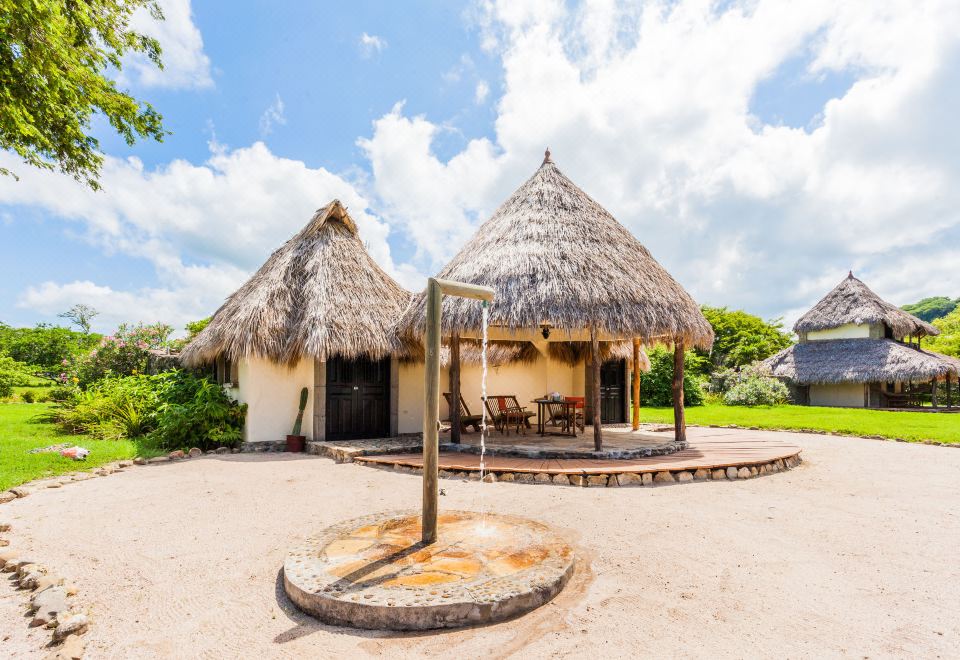 a small hut with a thatched roof is surrounded by gravel , and two chairs on the ground at Hotel Punta Teonoste