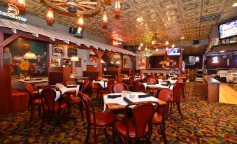 a large , well - lit restaurant with multiple dining tables and chairs , as well as a tv screen on the wall at Best Western Plus Longbranch Hotel  Convention Center