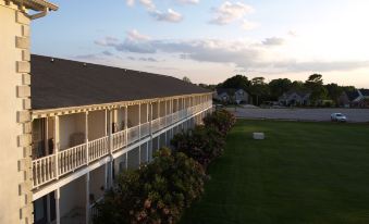 a long , white building with a brown roof is surrounded by green grass and trees at Beau Rivage Golf and Resort