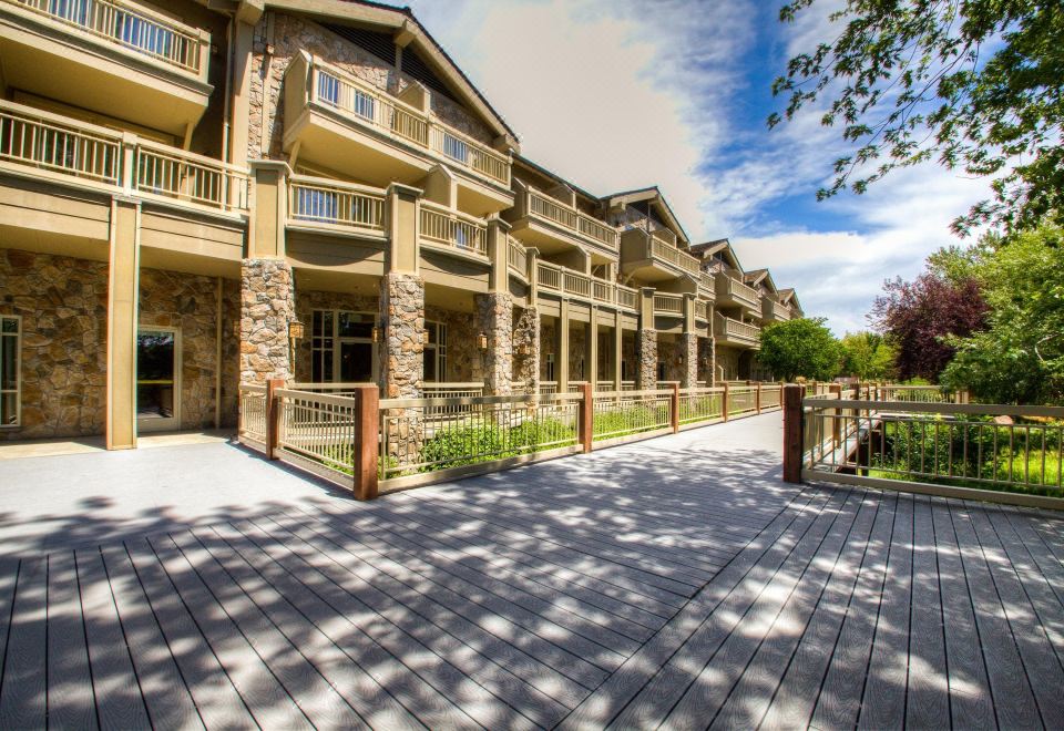 a large stone building with a wooden walkway leading to it , surrounded by trees and grass at Hilton Garden Inn Boise/Eagle