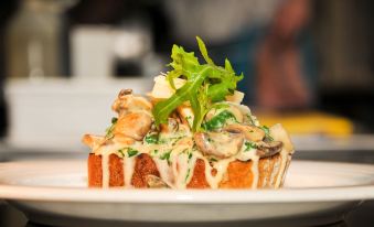 a white plate with a sandwich on top of it , topped with various toppings such as mushrooms and cheese at Mondo Hotel