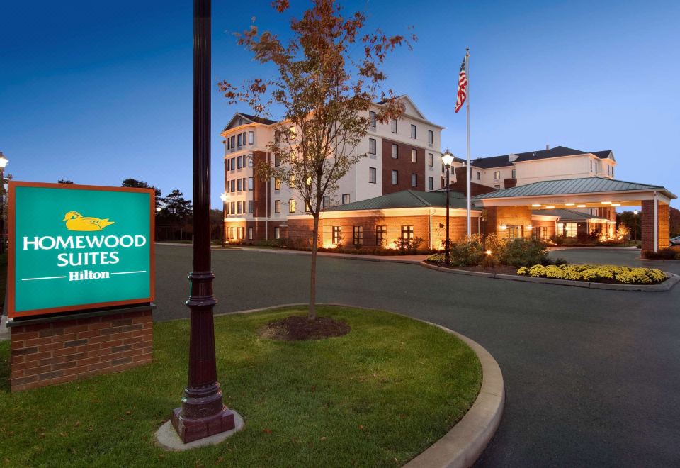 a large hotel with a sign in front of it , illuminated by lights and surrounded by trees at Homewood Suites by Hilton Newtown - Langhorne