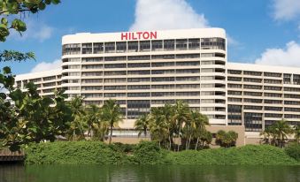 a hilton hotel with its name displayed prominently , surrounded by palm trees and a body of water at Hilton Miami Airport Blue Lagoon
