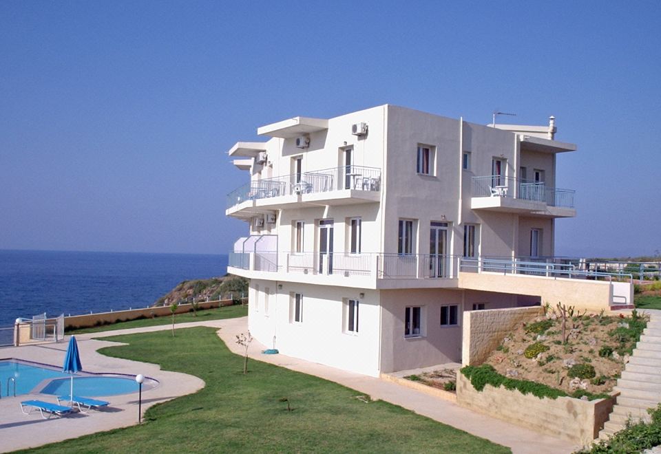 a large , two - story white building situated near the ocean , with a pool in front of it at Renieris Hotel