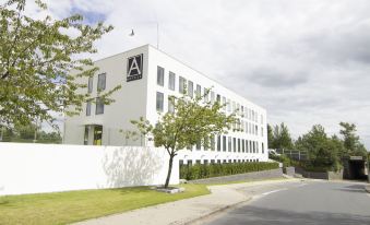 "a white building with a black "" a "" on the front is surrounded by trees and grass" at A Hotels Glostrup