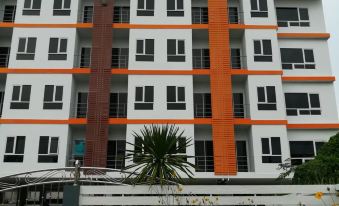 a modern apartment building with orange and white exterior accents , surrounded by greenery and flowers at V at Panus