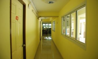 a long , narrow hallway with yellow walls and white tiles , leading to a room with a window at Sirasit 999 Mansion
