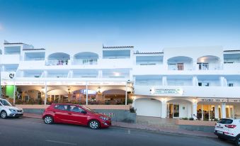 a red car is parked in front of a building with white windows , under a clear blue sky at Typic Oasis Sa Tanca