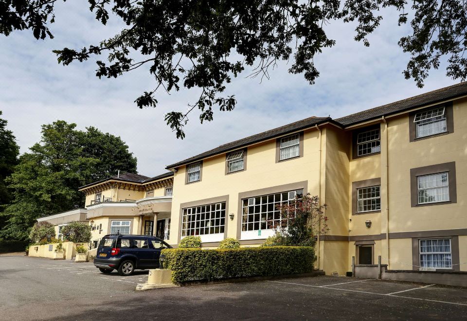 a yellow building with a black car parked in front , under a tree branch and under a clear sky at Reigate Manor Hotel