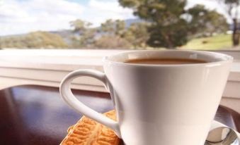a white coffee cup and saucer with a spoon on a wooden table , next to a window overlooking the outdoors at City View Motel