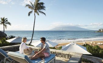a man and a woman are sitting on lounge chairs by the ocean , enjoying each other 's company at Four Seasons Resort Maui at Wailea