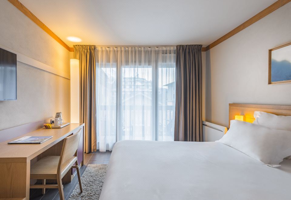a hotel room with a white bed , desk , and window curtains , providing a comfortable accommodation at Hotel le Morgane