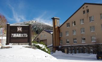 a snow - covered courtyard with a large building , possibly a hotel or resort , surrounded by trees at Manza Kogen Hotel
