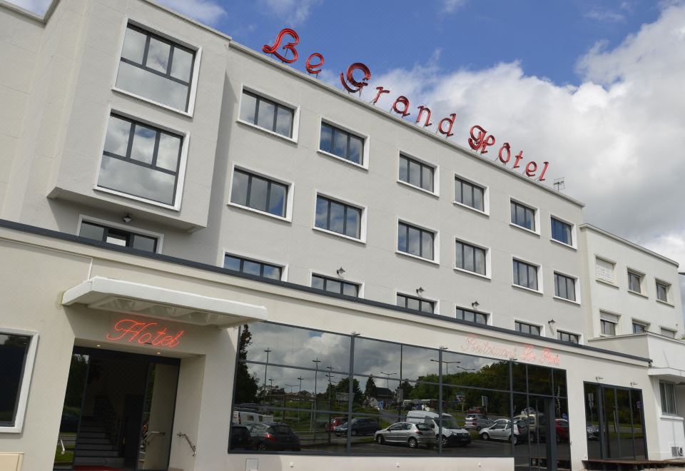 "a white building with the words "" be grand hotel "" prominently displayed on its side , surrounded by trees and cars" at Le Grand Hotel