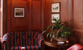 a cozy living room with wooden walls , a red chair , and a coffee table , decorated with plants and books at Overwater Hall