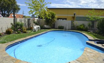 a backyard with a blue swimming pool surrounded by green grass , trees , and a fence at Colac Mid City Motor Inn