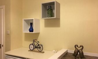 a small kitchen with a white table and two white shelves holding various items such as vases and a bicycle at Union Apartments