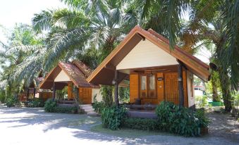 two small wooden houses with thatched roofs surrounded by palm trees , located on a dirt road at Nampueng Resort