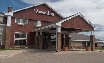a modern hotel building with an awning , surrounded by trees and a parking lot , under a cloudy sky at AmericInn by Wyndham Mounds View Minneapolis