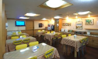 a large dining room with yellow chairs and tables , a tv on the wall , and a counter at Laurel Hotel