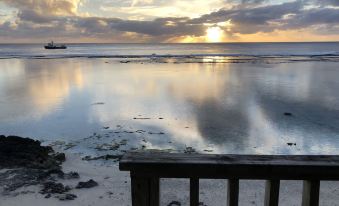 a serene beach scene at sunset , with the sun setting over the ocean and reflecting on the water at Mangaia Villas