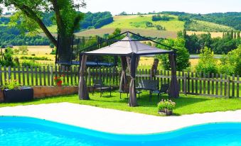 a backyard with a pool , outdoor furniture , and a gazebo , surrounded by green grass and trees at La Belle Verte