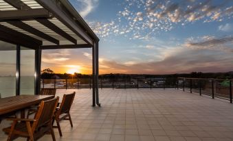 a patio with a table and chairs under a pergola , overlooking a beautiful sunset over the ocean at The Penthouse
