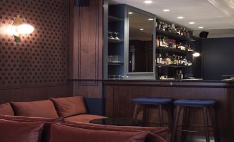 a well - lit bar area with two couches and a bar counter , surrounded by bottles and glasses on the shelves at Hotel Bachaumont