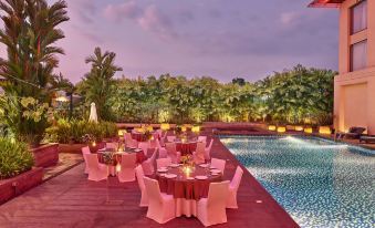 a beautifully decorated outdoor dining area with pink tablecloths and white chairs near a swimming pool at Courtyard Kochi Airport