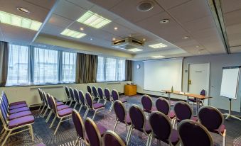 a conference room with purple chairs arranged in rows , a projector screen on the wall , and a whiteboard at Novotel Tours Centre Gare