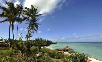 a tropical beach scene with palm trees , flowers , and the ocean in the background under a partly cloudy sky at The Residence Zanzibar