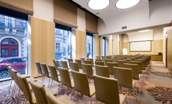 a large conference room with rows of chairs arranged in a semicircle , and a projector screen mounted on the wall at Hotel Moments Budapest