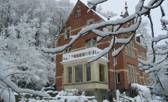 a large , red brick house with a white balcony and arched windows is surrounded by snow - covered trees at New-Castle