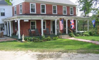 a red brick house with white trim , surrounded by a green lawn and a flag hanging from the porch at The Birchwood Inn