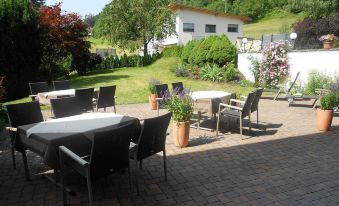 an outdoor dining area with several tables and chairs , surrounded by trees and a house at Hotel Königsblick by Keyone