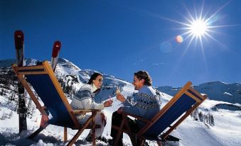 a man and a woman are sitting in beach chairs on a snow - covered hillside , enjoying each other 's company while sipping drinks at Hotel Königsblick by Keyone