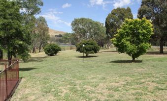 a grassy field with trees and a lake in the background , creating a serene atmosphere at Bonnie Doon Hotel