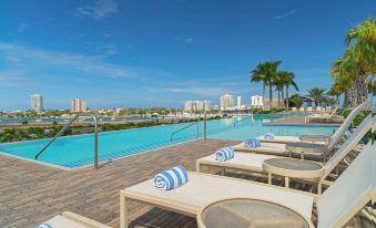 a large swimming pool with lounge chairs and palm trees , surrounded by a city skyline in the background at Sheraton Puerto Rico Resort & Casino