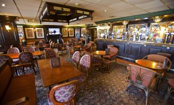 a well - decorated pub with wooden tables and chairs , a bar , and a tv in the background at Highfield Hotel