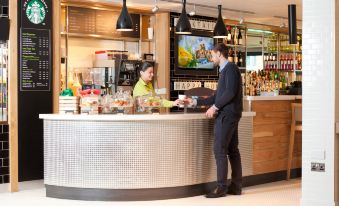 a man and a woman are standing behind a counter in a restaurant , interacting with the bartender at Holiday Inn London - Brentford Lock