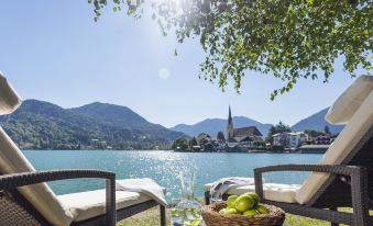 a serene scene of two lounge chairs placed near a body of water , with a basket of fruit nearby at Althoff Seehotel Uberfahrt