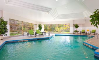 an indoor swimming pool with a large window , surrounded by chairs and lounge areas , in a well - lit room at Holiday Inn Laval - Montreal