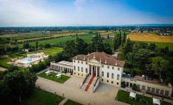 aerial view of a large white mansion surrounded by green fields , with a soccer field in the background at Hotel Villa Cornér Della Regina