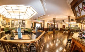 a large , well - lit restaurant with multiple dining tables and chairs , as well as a bar area at Bredbury Hall Hotel