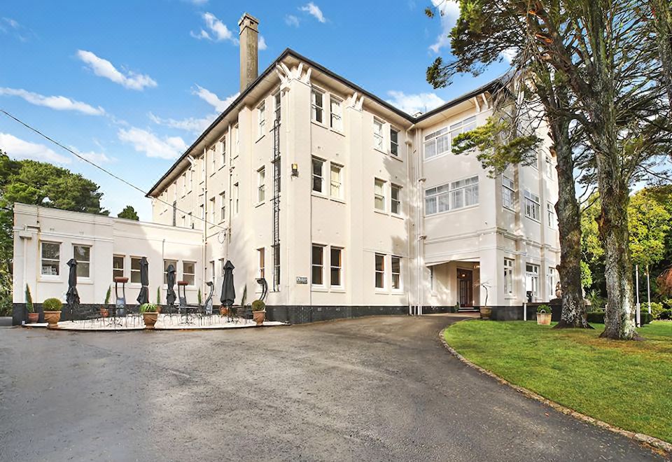 a large white building with a tall chimney is surrounded by trees and a gravel driveway at The Robertson Hotel