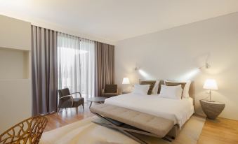 a large bed with a gray headboard is in the center of a room with white walls and windows at Torre de Gomariz Wine & Spa Hotel