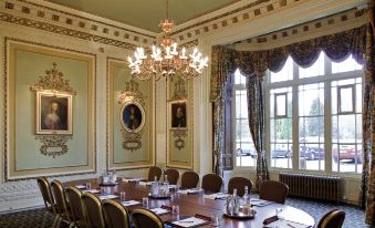 a formal dining room with a round table surrounded by chairs , and a chandelier hanging from the ceiling at Mercure Blackburn Dunkenhalgh Hotel & Spa