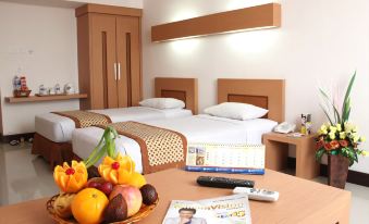a hotel room with two beds , a dining table , and a plate of fruit on it at Ceria Hotel Jambi by Tritama Hospitality