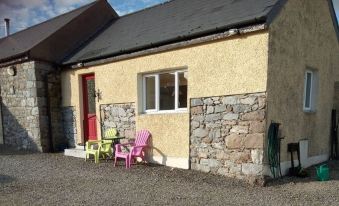 a stone house with two chairs and a table in front of it , situated on a gravel driveway at Brigadoon