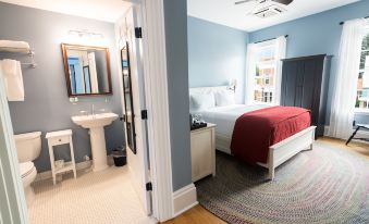 a modern bedroom with blue walls , white beds , and a red bedspread , connected to a bathroom with a sink and toilet at The Cadillac House